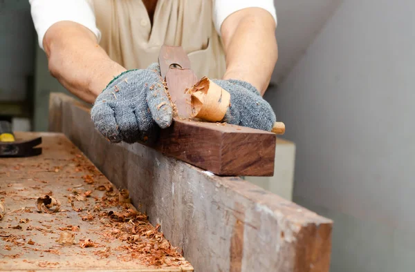 Carpenter\'s hands planing a plank of wood with a hand plane