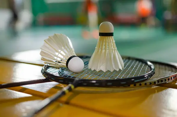 Badminton rackets and white cream badminton shuttlecocks after playing or after games on green floor in indoor badminton court  soft focus  concept for badminton lovers around the world.
