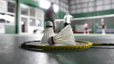 Badminton raketleri ve beyaz kremalı badminton mekikleri oynadıktan sonra ya da yeşil zeminde dünya çapında badminton severler için kapalı badminton kortunun yumuşak odaklanma konseptinde oynadıktan sonra..