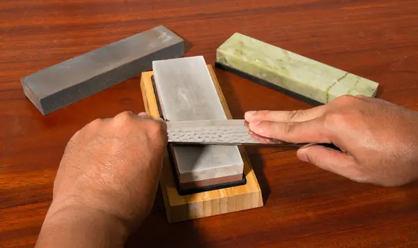 stock image Craftsman sharpening knives on a Japanese whetstone, on a wooden table