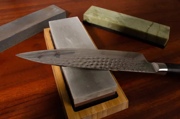 stock image Craftsman sharpening knives on a Japanese whetstone, on a wooden table