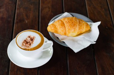 Kapuçino ahşap masa üzerinde kruvasan ile kahve fincan