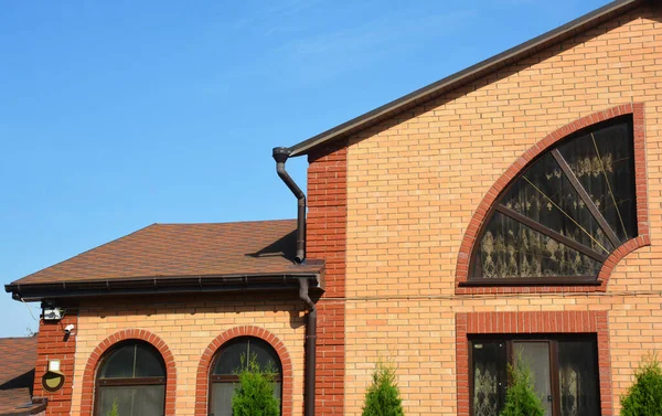 Close up on asphalt shingles brick house rooftop with rain gutter pipeline system.