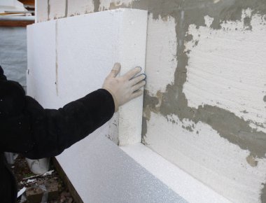 House exterior wall foam insulation. A close-up of a building contractor installing a rigid foam, styrofoam insulation on the concrete block house wall.