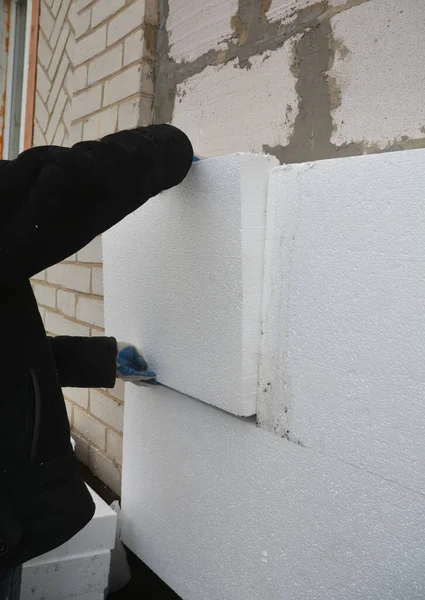 House exterior wall foam insulation. A close-up of a building contractor installing a rigid foam, styrofoam insulation on the concrete block house wall.