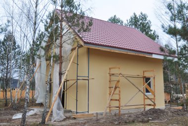 White uPVC fascia boards installation along the roofline of the house. New house with metal roof, painted walls under construction.