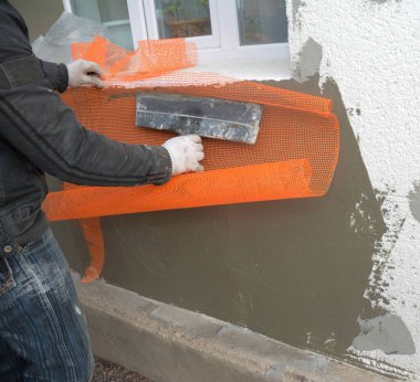 Rigid foam sheathing. Contractor plastering wall with fiberglass mesh, plaster mesh after exterior house wall rigid insulation.  Exterior Sheathing Foam Board Insulation