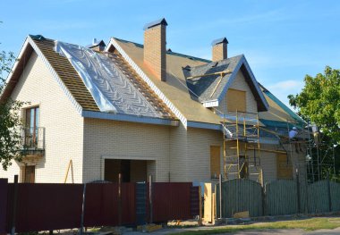 Roofing construction. Roofer contractors laying asphalt shingles on brick house rooftop.