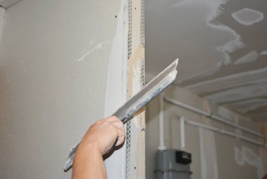 Builder plastering, skim coating, finishing, applying the first coat of plaster on a drywall partition wall  during house renovation. 