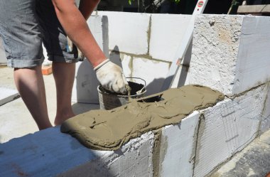 Builder contractor laying white autoclaved aerated concrete AAC blocks with concrete during house blocks wall construction.
