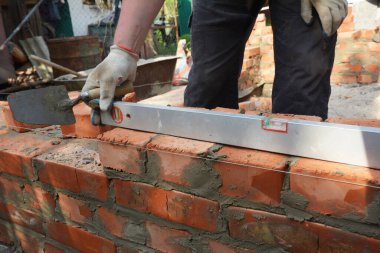 Builder contractor laying bricks and measure new house wall with spirit level.