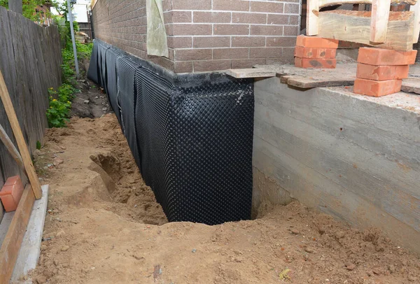Basement waterproofing with dimple mat, dimple drain in problem corner area. House  foundation wall insulation with rigid foam board, waterproofing membrane and house foundation construction trench.