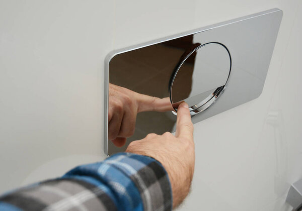 A man is pressing a wall-mounted polished chrome single flush plate to flush the toilet.