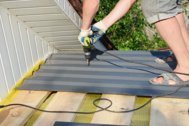 Çatı müteahhidi elektrikli matkapla evin çatısına metal çatı örtüsü seriyor. Çatı inşaatı.