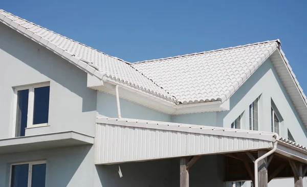 White tiled roof house with rain gutter pipeline, soffits and waterproofing in problem area. Roofing construction.