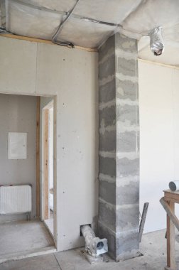 Tamamlanmamış bir ev inşaatı hakkında içeriden bir bakış. Bir baca gemisinin içine yerleştirilmiş bir sabun taşı çakmağı, havalandırma boruları, elektrik kabloları ve tavan yalıtımı.. 