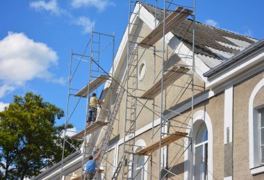 KYIV, UKRAINE - November 22, 2023: Building contractors on scaffoldings are rendering, applying stucco, renovating external walls, the facade of a house with asbestos roof. 
