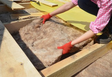 Çatı yapımında DIY: koruyucu eldivenli bir kadın ev inşaatının metal çatısına cam yün, mineral yünü veya battaniye termal yalıtımı yerleştiriyor.