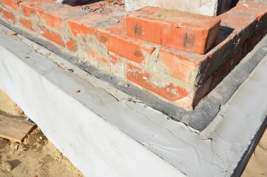 Temeli su sızıntılarından korumak için nemli su geçirmez zarı olan yalıtımlı temelin üzerine tuğla duvar örmek..