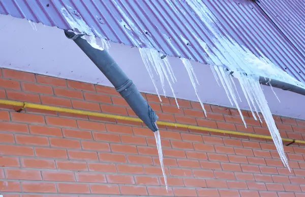 Rain gutter damage in winter when water freezes, turns into icicles on the roof, breaks the roof gutter of the house and becomes dangerous. Icicles hanging from the roof and falling on people.