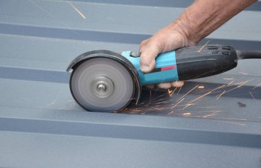 Roofer Conuctor bir güç açı öğütücüsüyle kıvrımlı metal çatı kaplaması kesiyor. Metal çatı fayansları kesiliyor.