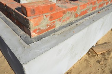 Yeni ev inşaatının temelindeki tuğla duvarın su geçirmez olduğu yakın plan.