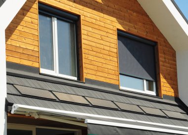 Tavan arası pencerelerinde geri çekilebilir güneş gözlüğü ve güneş kremleri. Geri çekilebilir Güneş Ekranları ve geri çekilebilir tentelerle modern ahşap ev cephesi.