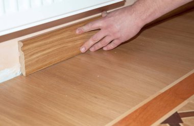 Adam ahşap bir kaide yapıştırıyor, yeni ahşap bir parkede tahtadan sıyrılıyor.