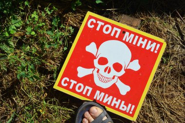 Adam Ukrayna mayınının tehlike işaretine bastı. Mayınları durdur Ukraynaca ve Rusça metin ve kafatası simgesi.  