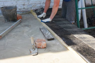 Bir müteahhit, temelini sonraki tuğla işinden ayırmak için su geçirmez bitumen bant yerleştirir. Ev temelinde asfalt su yalıtımı.