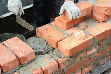 Tuğla örme teknikleri. İnşaatçı tuğla döşeme malası, tuğla ve betondan duvar inşa ediyor.. 