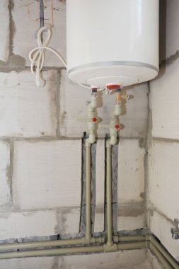 Elektrikli kazan kurulumu ve duvardaki deliklere plastik borular yerleştirilmesi. Sıcak ve soğuk su boruları olan elektrikli kazan..