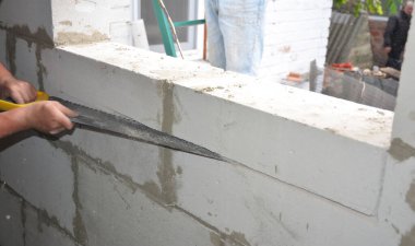 İnşaatçılar havalandırma beton duvarının penceresini testereyle kesiyorlar.