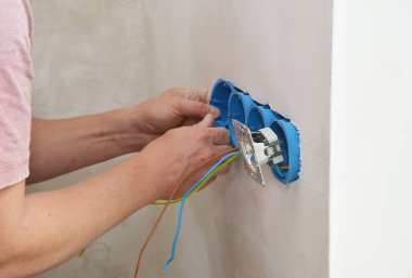 Elektrikçi duvardaki elektrik kutularına yeni prizler kuruyor.