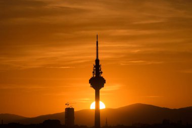 Gün batımında, güneş dağların ardında ve bir iletişim kulesinin tepesinde batıyor. Madrid 'in gökyüzünde turuncu tonlarda bulutlar....