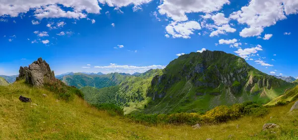 Dağ zirvesinden panoramik bir vadi manzarası. Bulutlu mavi gökyüzü. Yeşil dağ duvarları ve sonsuz gökyüzünün arkaplanı. Ön planda bir kaya ve yerde bir sırt çantası..
