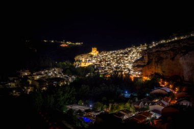 Alcala del Jucar, Albacete, İspanya; 1 Mayıs 2024: Panoramik gece fotoğrafı, sokak lambalarıyla aydınlatılmış Alcala del Jucar 'ın bakış açısı, dağdaki evler ve Albacete kalesi. İspanya