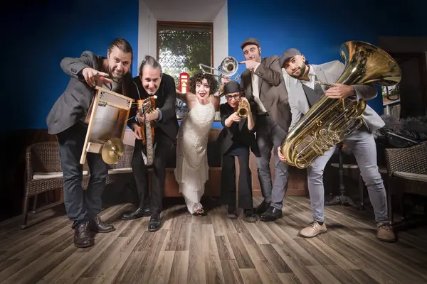 Retro kostümler giymiş caz grubu, çömelmiş bir grup olarak kameraya bakarken, enstrümanlarını ileri doğru işaret ediyorlar. Caz kulübü atmosferinde bir geçmişi var..