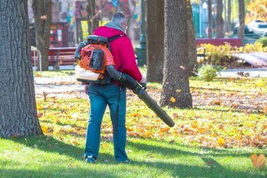 Şehir parkında ağır yaprak üfleyicisi çalıştıran bir işçi. Sonbaharda düşen yaprakları toplamak. Park temizleme servisi