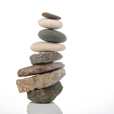 Beyaz zemin üzerinde istiflenmiş taşlar piramidi. Hayatta dengeleme ve denge