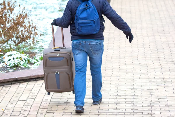 man walking down the sidewalk with a luggage bag
