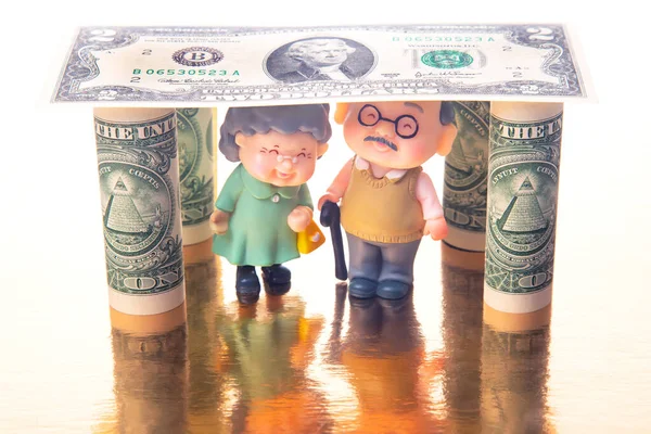 miniature people. a couple of pensioners under the house of dollars. financial security and pension for the elderly. concept of financial independence