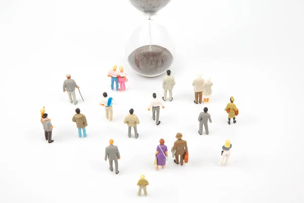 miniature people. different people are walking next to the hourglass on a white background. lifespan of humanity