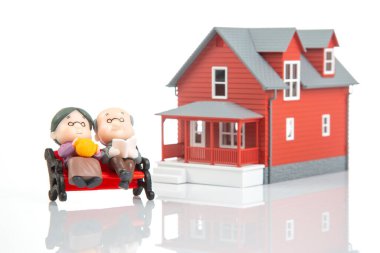 Minyatür insanlar. Beyaz bir arka planda ev modelinin yanında birkaç emekli insan var. Yaşlılar için finansal güvenlik ve emekli maaşı. Mali bağımsızlık kavramı
