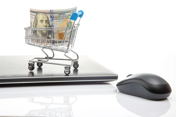 Model of a grocery cart with dollar money on the background of a laptop. Online business sale. Financial business success.