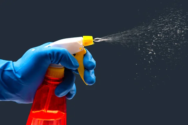 water sprayer bottle in a hand with gloves on a dark background with liquid spray. household items for home