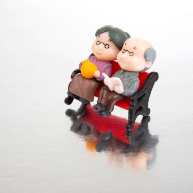 miniature people. figures for the concept. a couple of retired people are sitting together on a bench. old age and helping each other