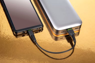 Powerbank altın arka planda bir akıllı telefondan para alıyor. Cihazları ve akıllı telefonları şarj etmek için elektronik aygıtlar