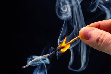 Karanlık bir arka planda yanıp tutuşan ahşap kibrit. Yanan bir ağaçtan gelen parlak ateş ve duman.