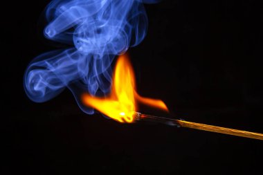 Karanlık bir arka planda yanıp tutuşan ahşap kibrit. Yanan bir ağaçtan gelen parlak ateş ve duman.